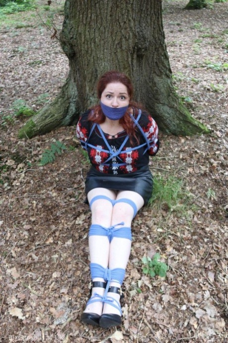 Pale redhead is silenced with a gag while tied up in her clothes under a tree 35774830