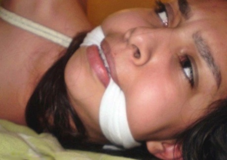 Dark-haired girl is cleave gagged and hogtied on a bed in a dress 62283024