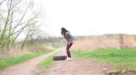 Solo girl Billie takes a piss over a tire on a dirt road in the country 89647812